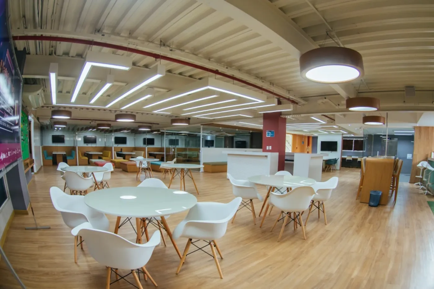 Espaço de coworking com forro metálico aparente, iluminação linear e estações de trabalho coletivas